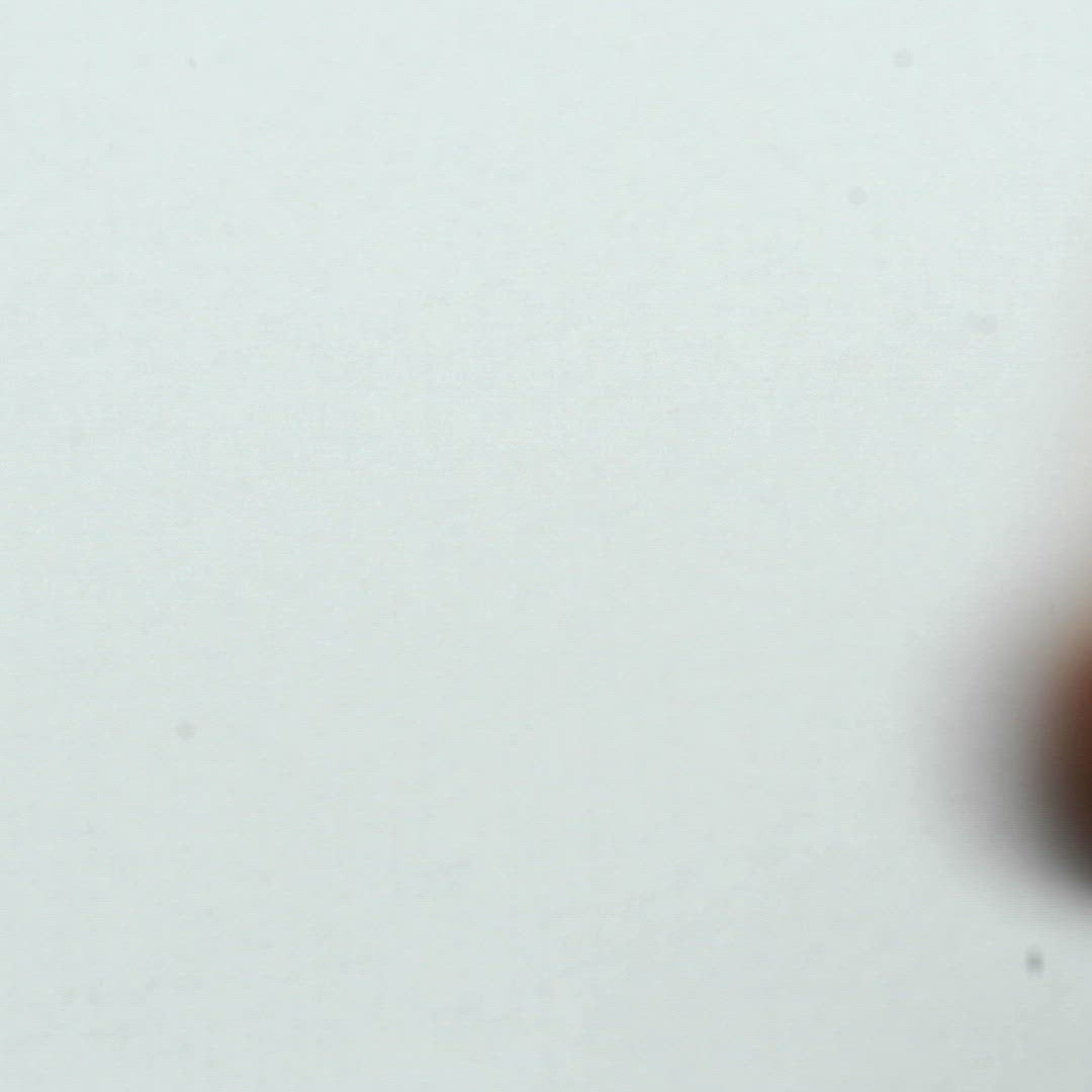 A closeup video of a man stamping on white paper, leaving the line art of a grinning clown skull with a pointy hat and frilly collar.