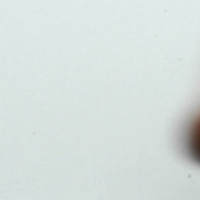 A closeup video of a man stamping on white paper, leaving the line art of a grinning clown skull with a pointy hat and frilly collar.