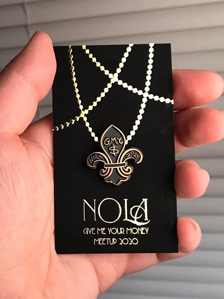 Black NOLA fleur de lis pin on its backer, held in a hand. Photo by Ali Meade.